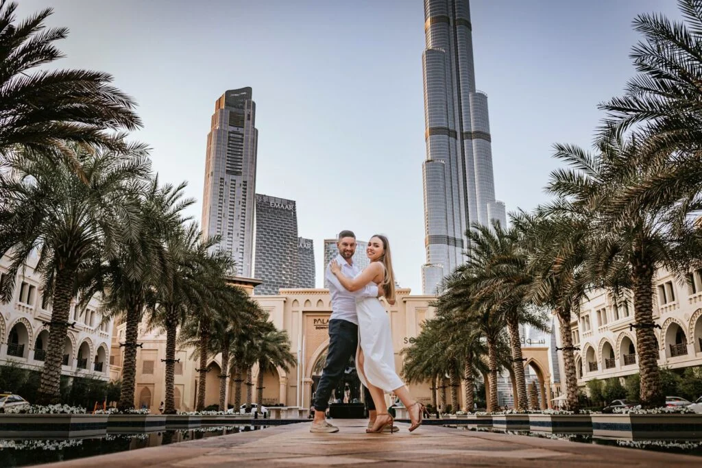 Couple embracing on a palm lined walkway with the Dubai skyline behind them