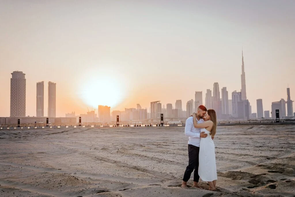 Couple embracing on open ground at sunset, the Dubai skyline on the horizon