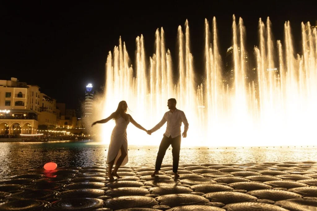 Couple holding hands in front of the illuminated fountains