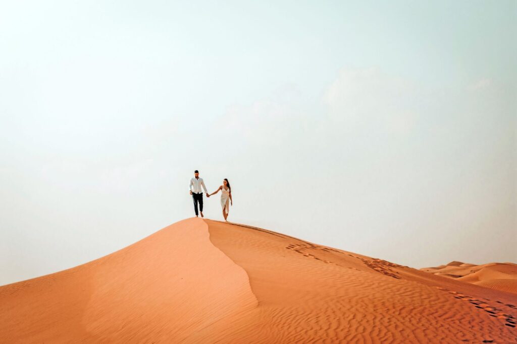 Couple walking along the crest of a dune against a pale sky
