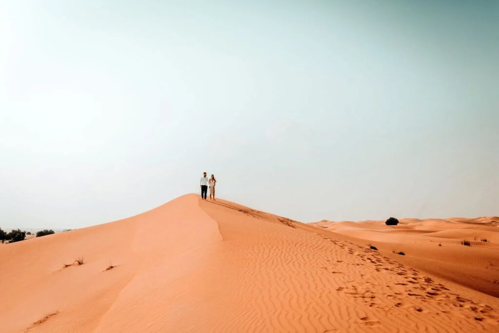Two figures small on a desert dune at dusk