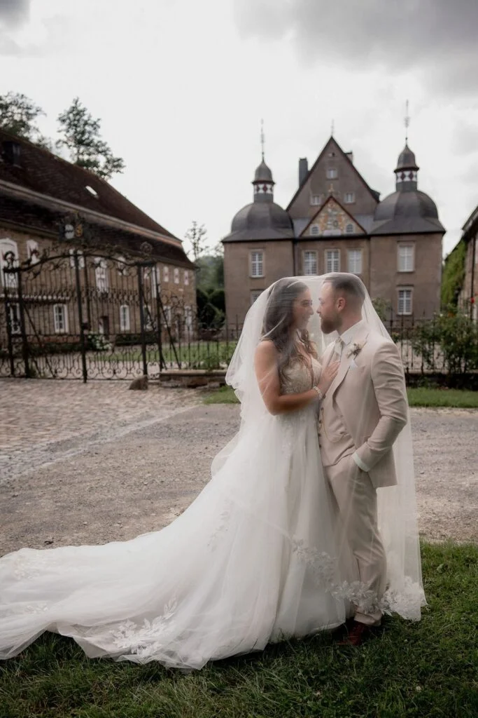 Bride and groom embracing on the lawn, her veil trailing across the grass