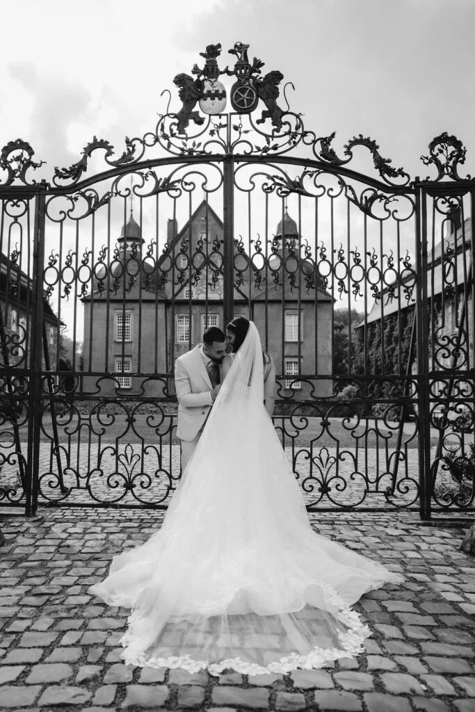 Black and white photograph of the couple at the castle gate, the bride's train on the cobbles