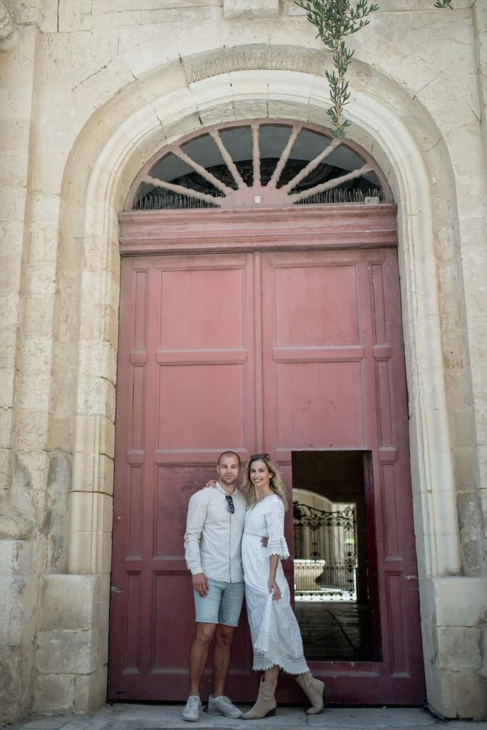 Couple in white standing in a tall pink doorway in Mdina, Malta