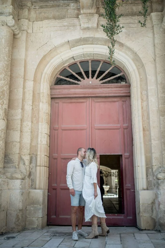 Couple kissing in the pink doorway of a limestone building in Mdina