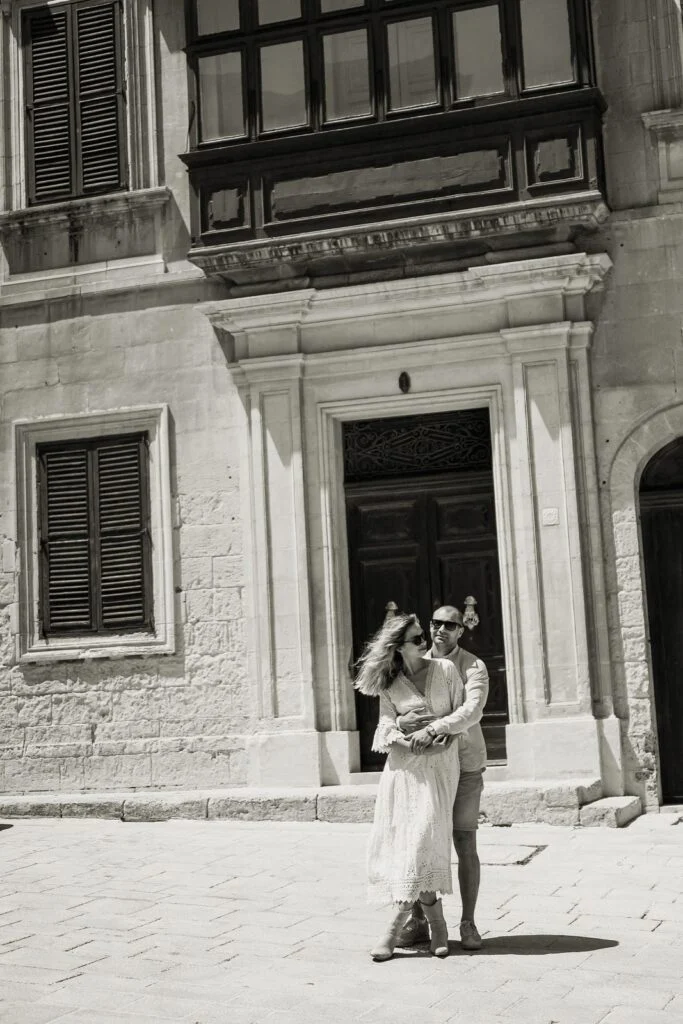 Black and white photograph of a couple on a limestone street beneath a closed balcony