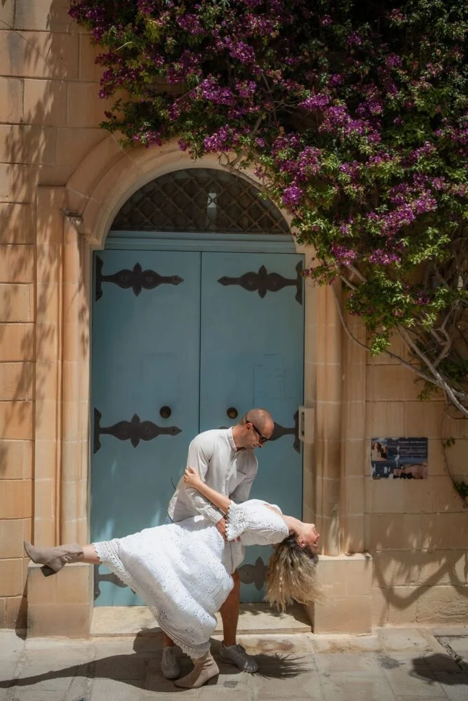 Man dipping his partner beneath bougainvillea beside a blue door