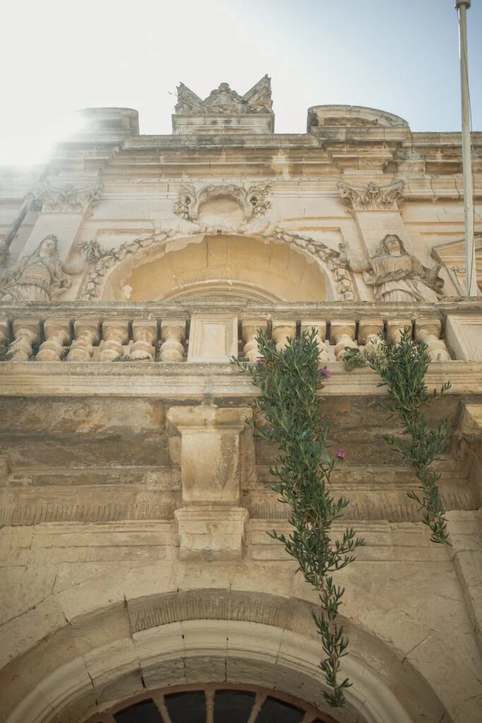 Carved limestone facade in Mdina with a cypress growing against it