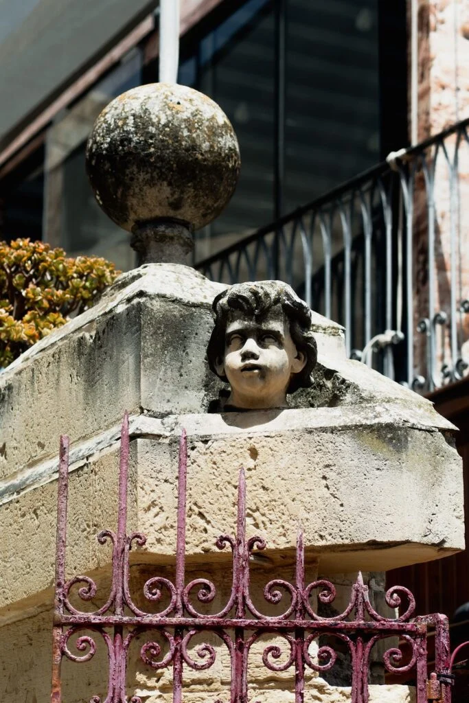 Stone cherub on a gatepost above a pink iron railing