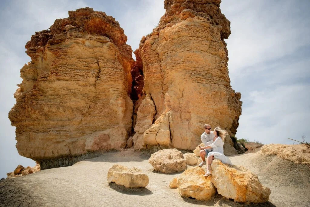 Couple sitting at the foot of golden rock formations by the sea