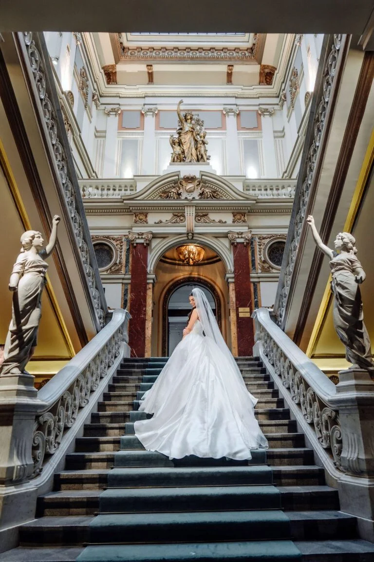 Bride seen from behind ascending the central staircase at Salon 1905, statues on either side