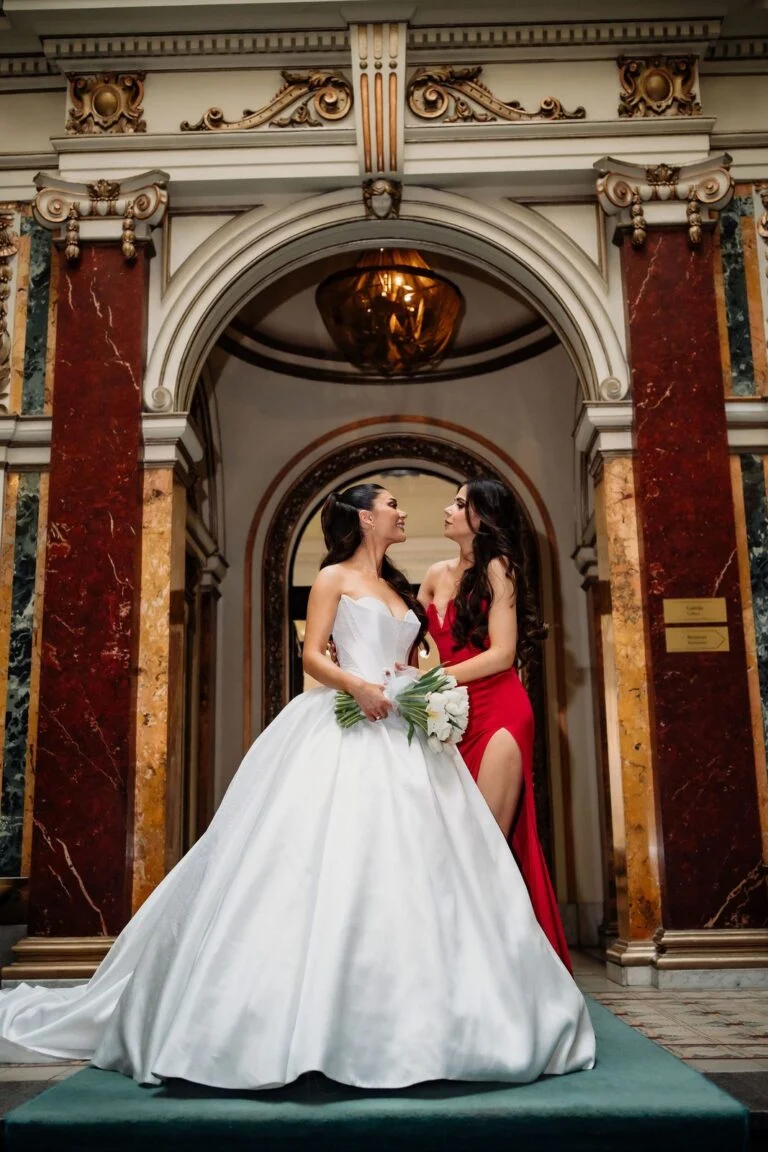 Bride and a woman in a red gown in the gilded doorway at Salon 1905