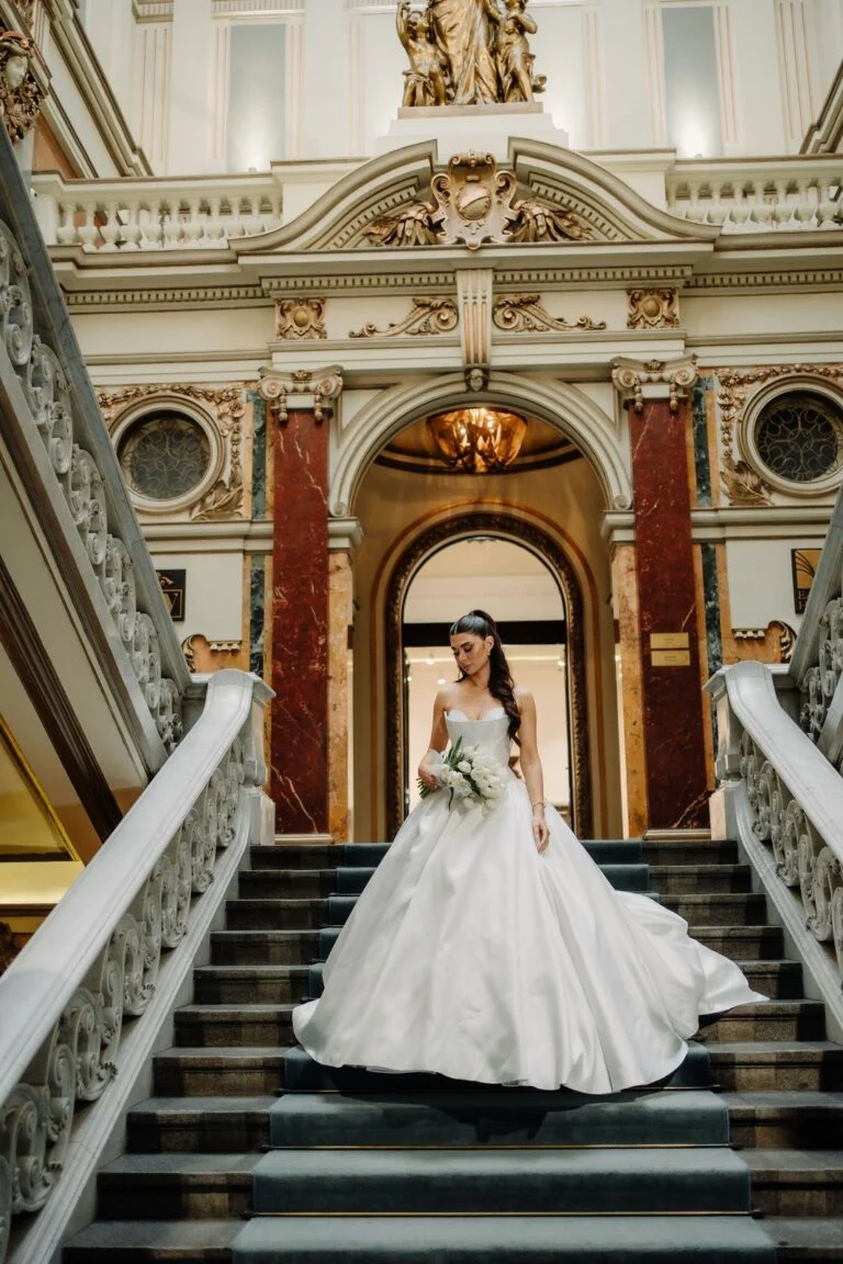 Bride centred at the foot of the marble staircase at Salon 1905, gilded ceiling above
