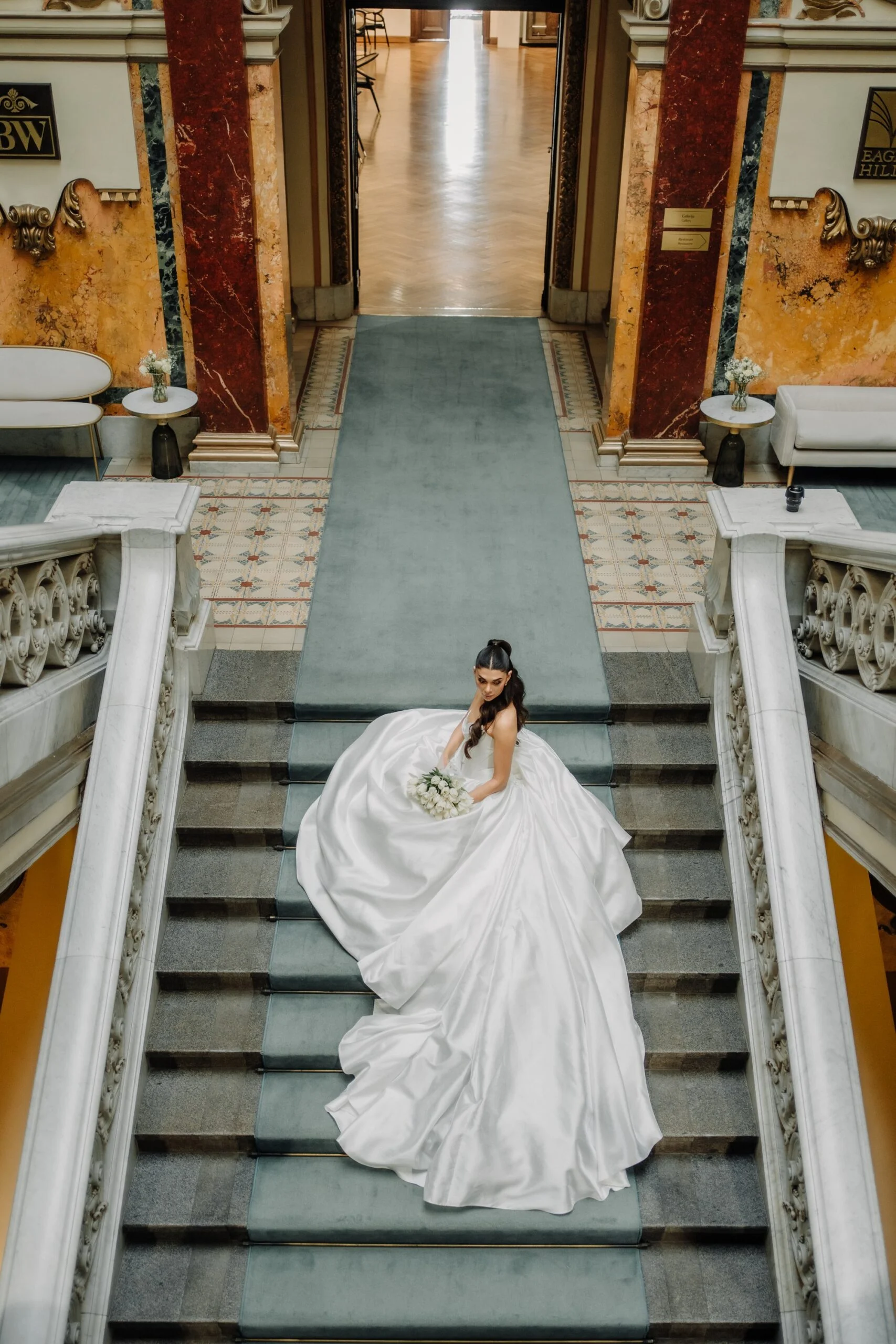 Bride centred at the foot of the marble staircase at Salon 1905, gilded ceiling above