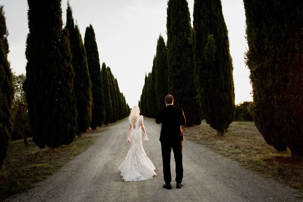 Bride and groom walking away down an avenue of cypress trees in Tuscany