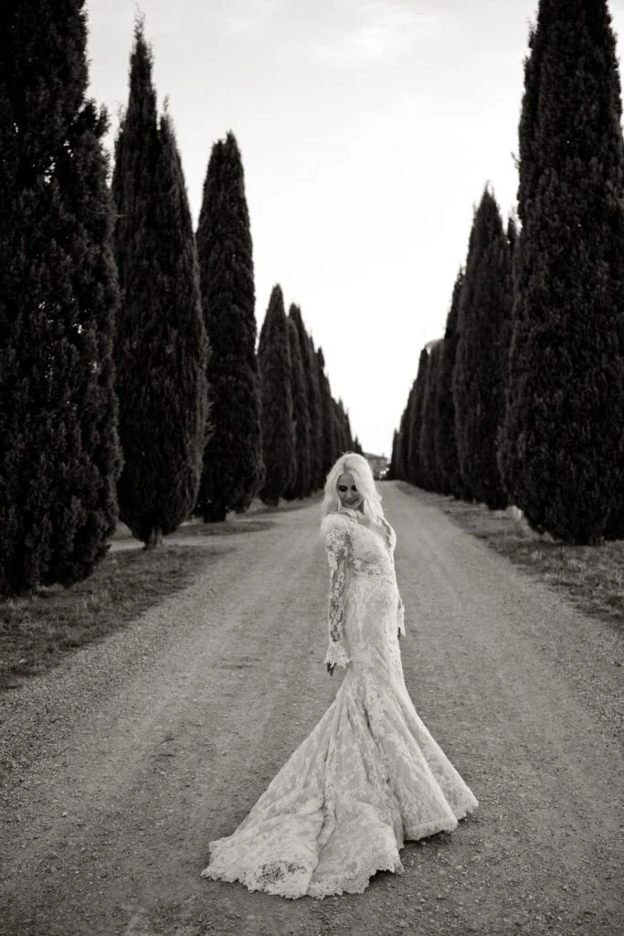 Black and white photograph of the bride on the gravel road between cypress trees
