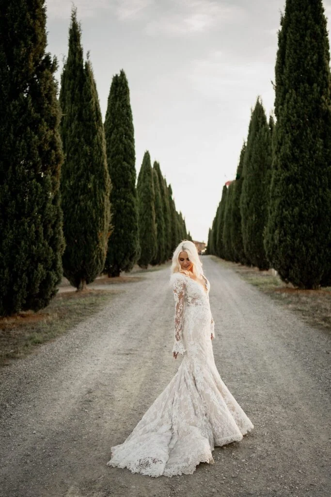 Bride on the cypress avenue at sunset, her train spread across the gravel