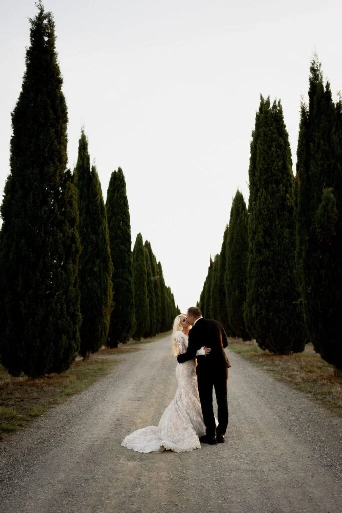 Bride and groom together on the gravel road between the cypresses