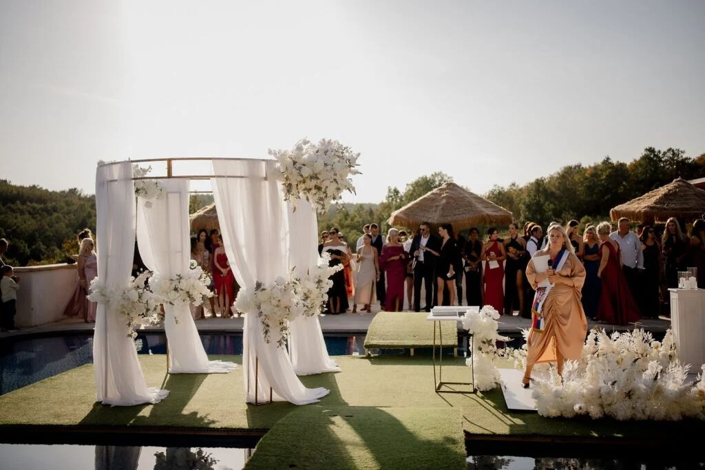 Ceremony arch reflected in the pool, guests seated around it