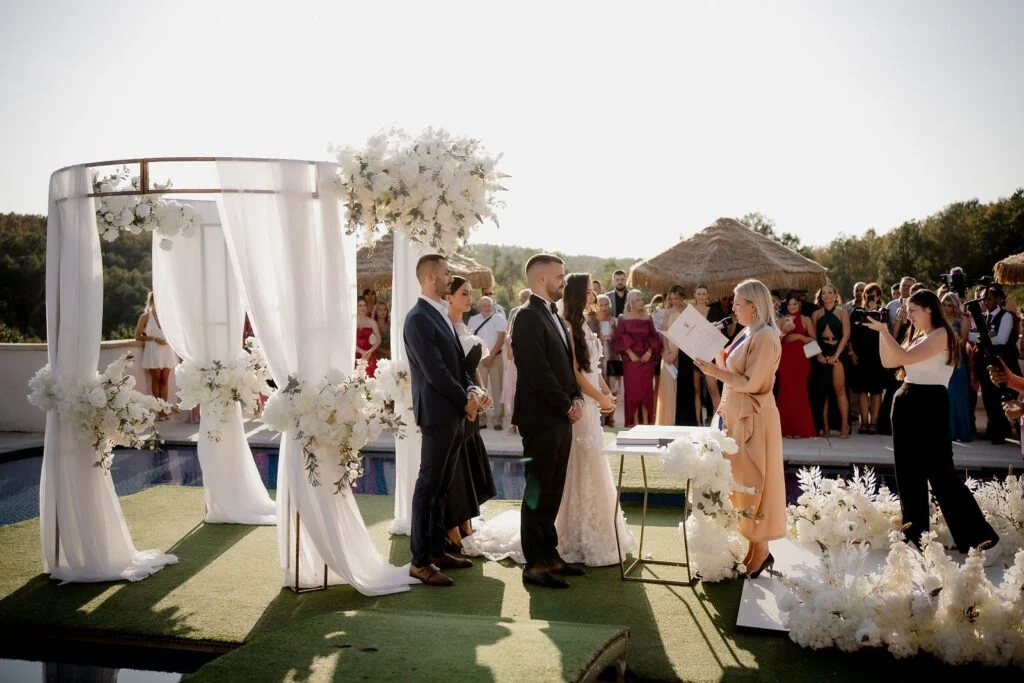 Bride and groom at the ceremony arch beside the pool