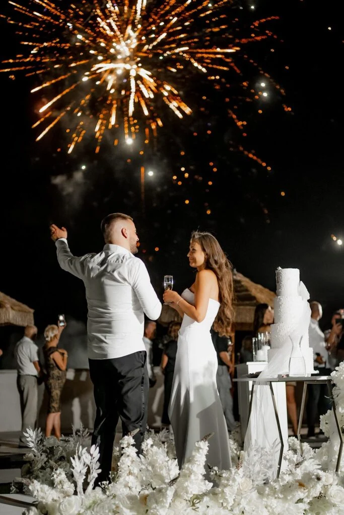 Groom raising his hand as fireworks burst above the terrace