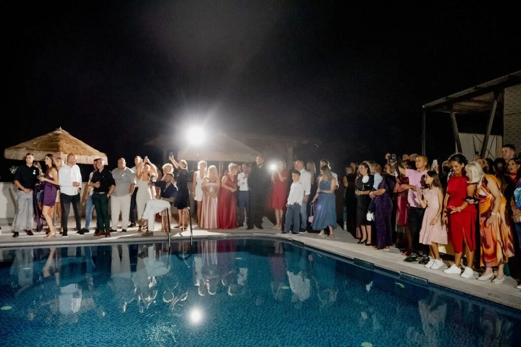 Guests standing around the lit swimming pool at night