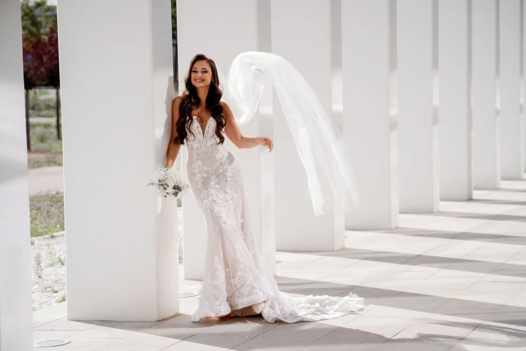 Bride with her veil lifted by the wind between the white columns
